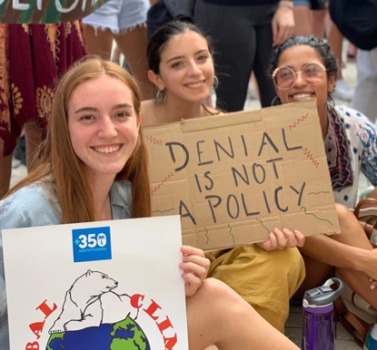 A group of people holding a sign posing for the cameraDescription automatically generated