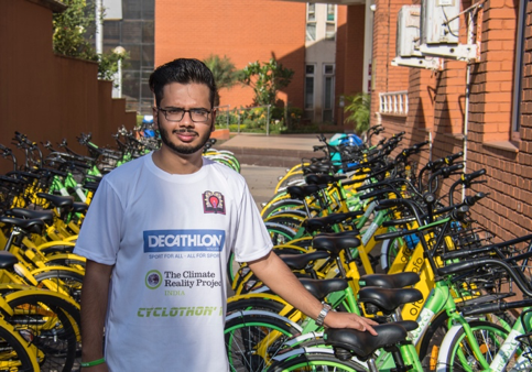 A person with a bicycle in front of a buildingDescription automatically generated